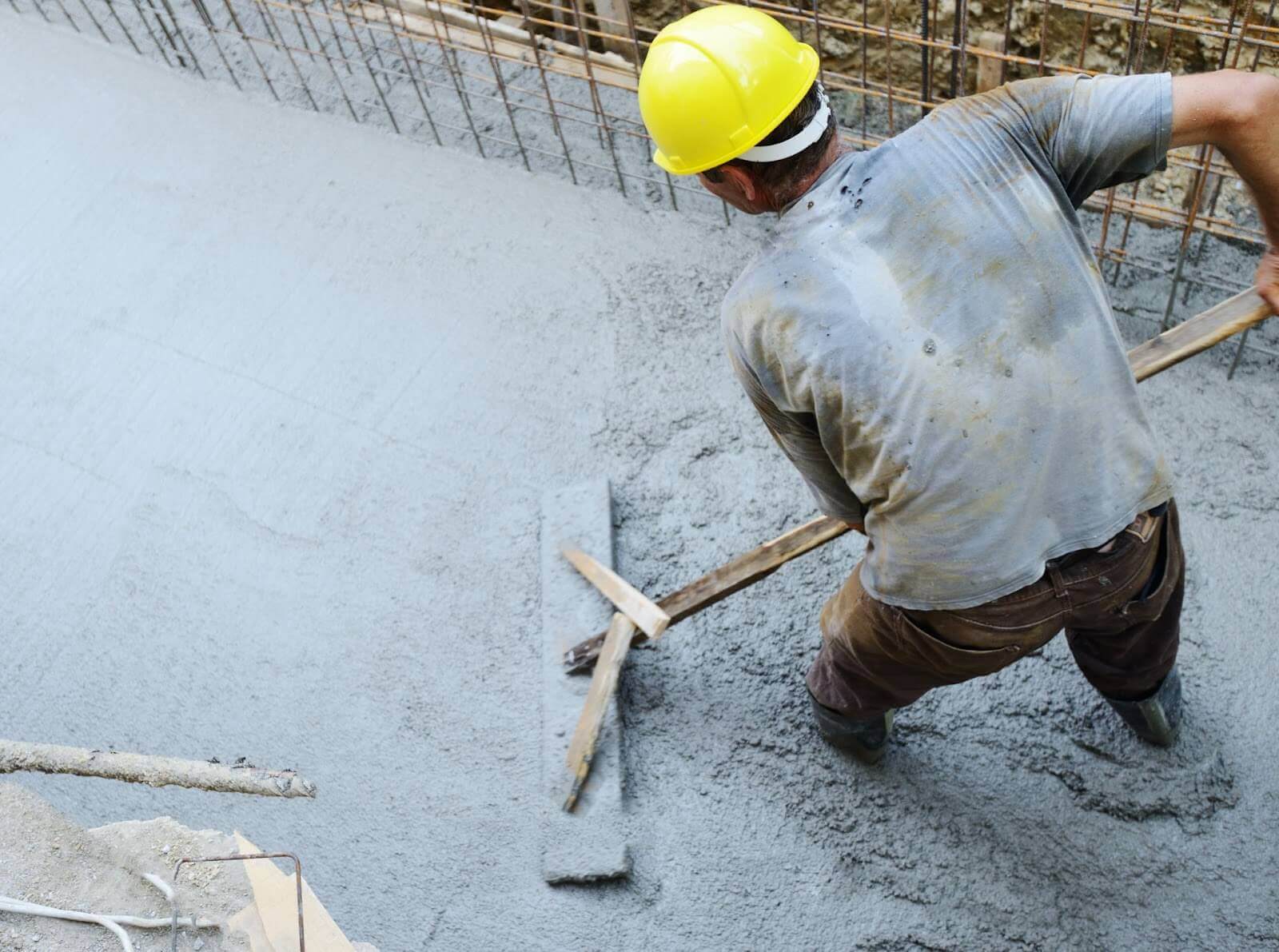Construction worker laying cement on ground with long trowel