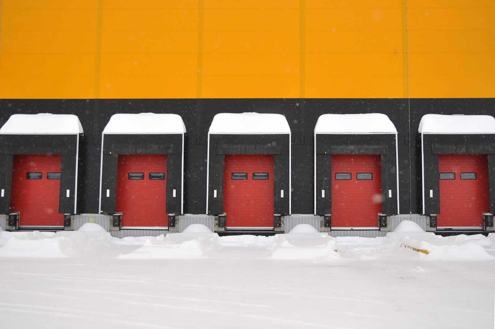 Yellow warehouse with five bays with red doors on a snowy day